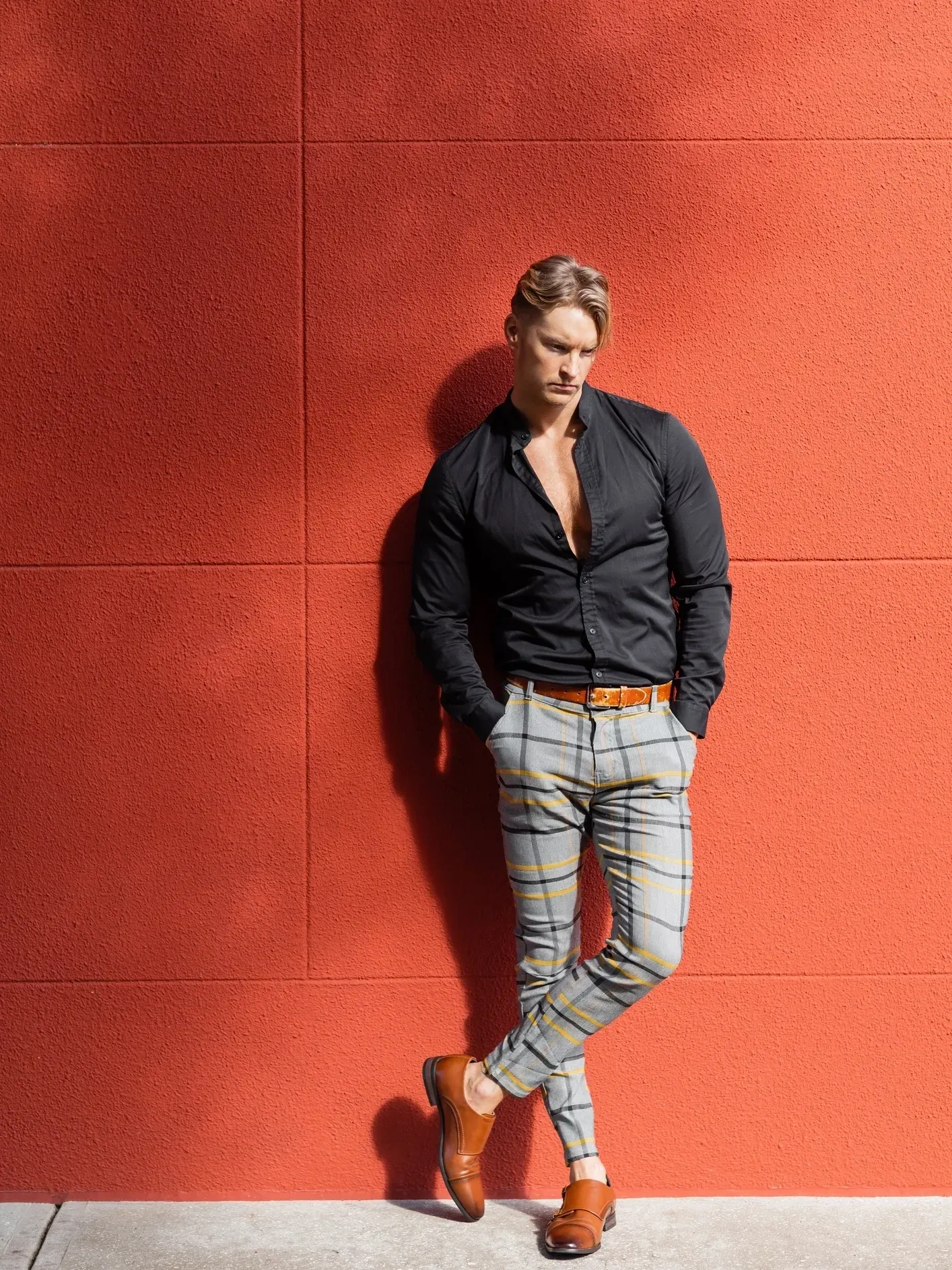 Man in stylish outfit against red wall.