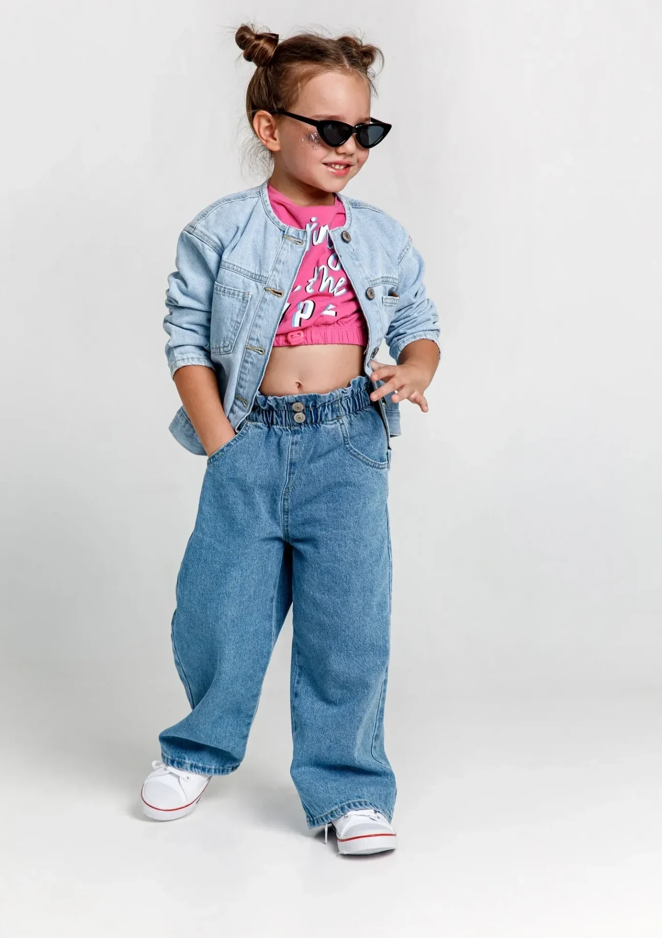 Child wearing denim outfit and sunglasses smiling.